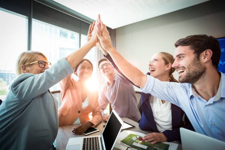 business people giving high five at desk in the office